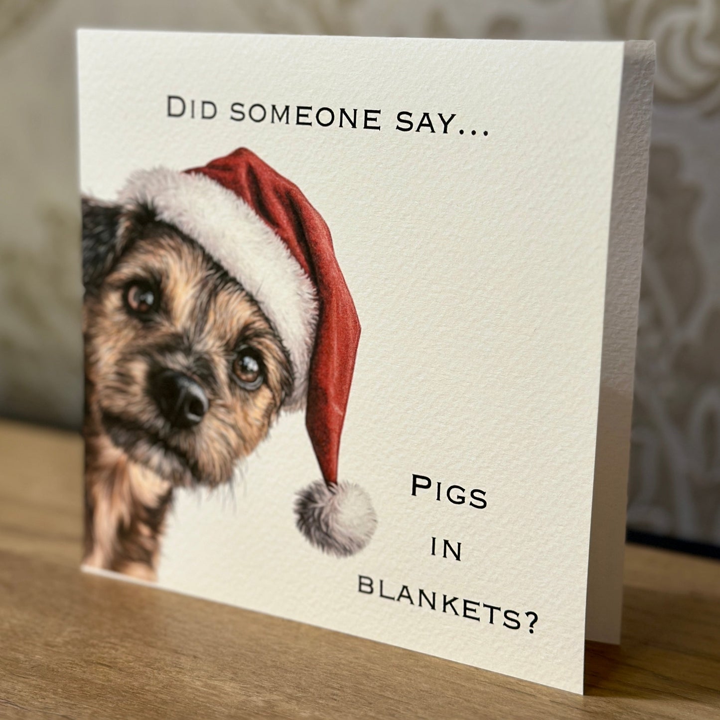 Card with a dog wearing a Santa hat and humorous text on a wooden surface.