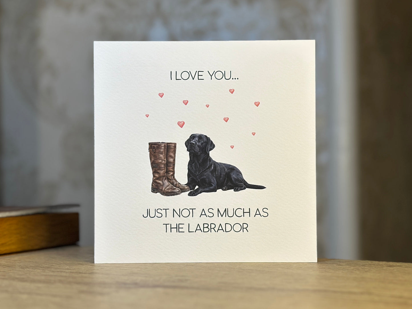 Card with illustration of a dog and boots, text 'I love you just not as much as the Labrador', on a wooden surface.