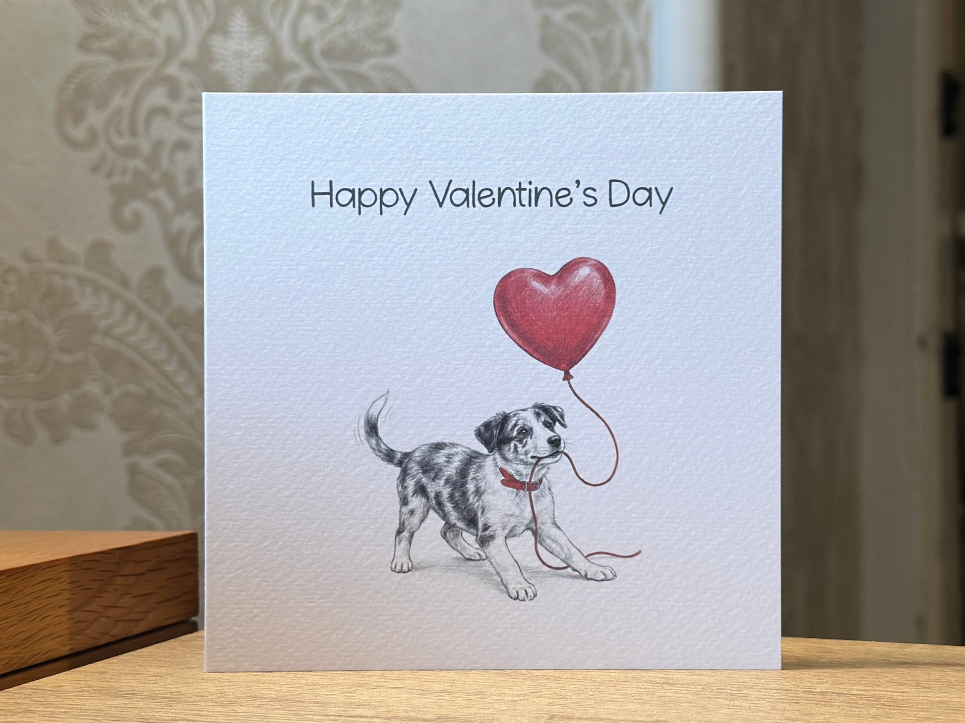 Valentine's Day card with a dog holding a heart balloon on a wooden surface.