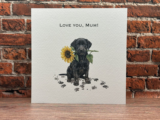 Drawing of a Black Labrador puppy sitting with muddy paw prints, holding a large yellow sunflower in its mouth with text reading Love You, Mum.