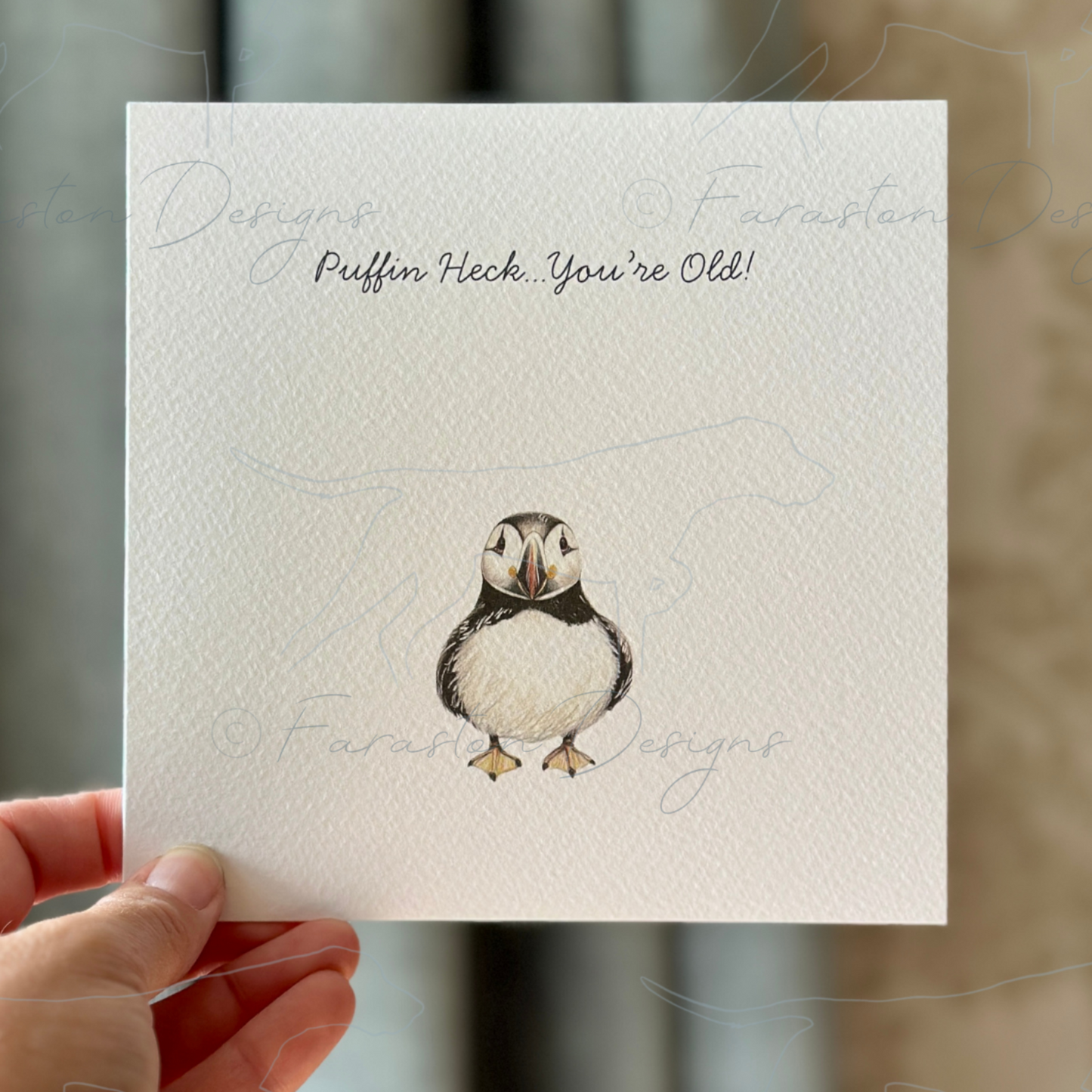 Hand holding a card with a puffin illustration and text against a neutral background