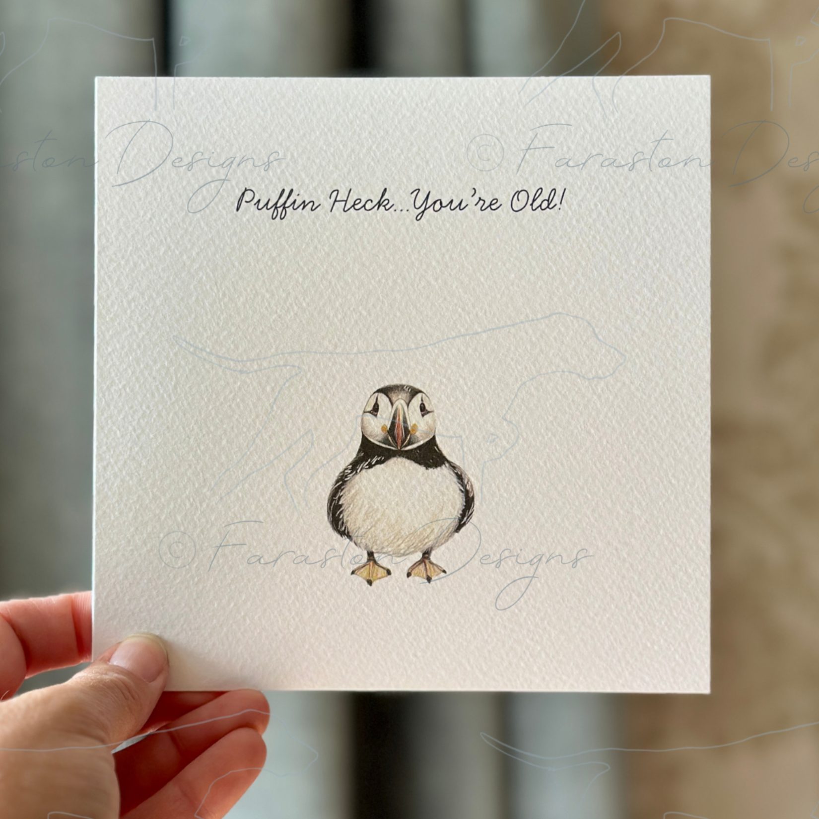Hand holding a card with a puffin illustration and text against a neutral background