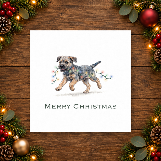 A square white Christmas greeting card featuring a watercolor illustration of a terrier dog carrying a string of lights in its mouth, with 'MERRY CHRISTMAS' printed below. The card is displayed on a rustic dark wood background, framed by festive greenery, pinecones, ornaments, and warm fairy lights.